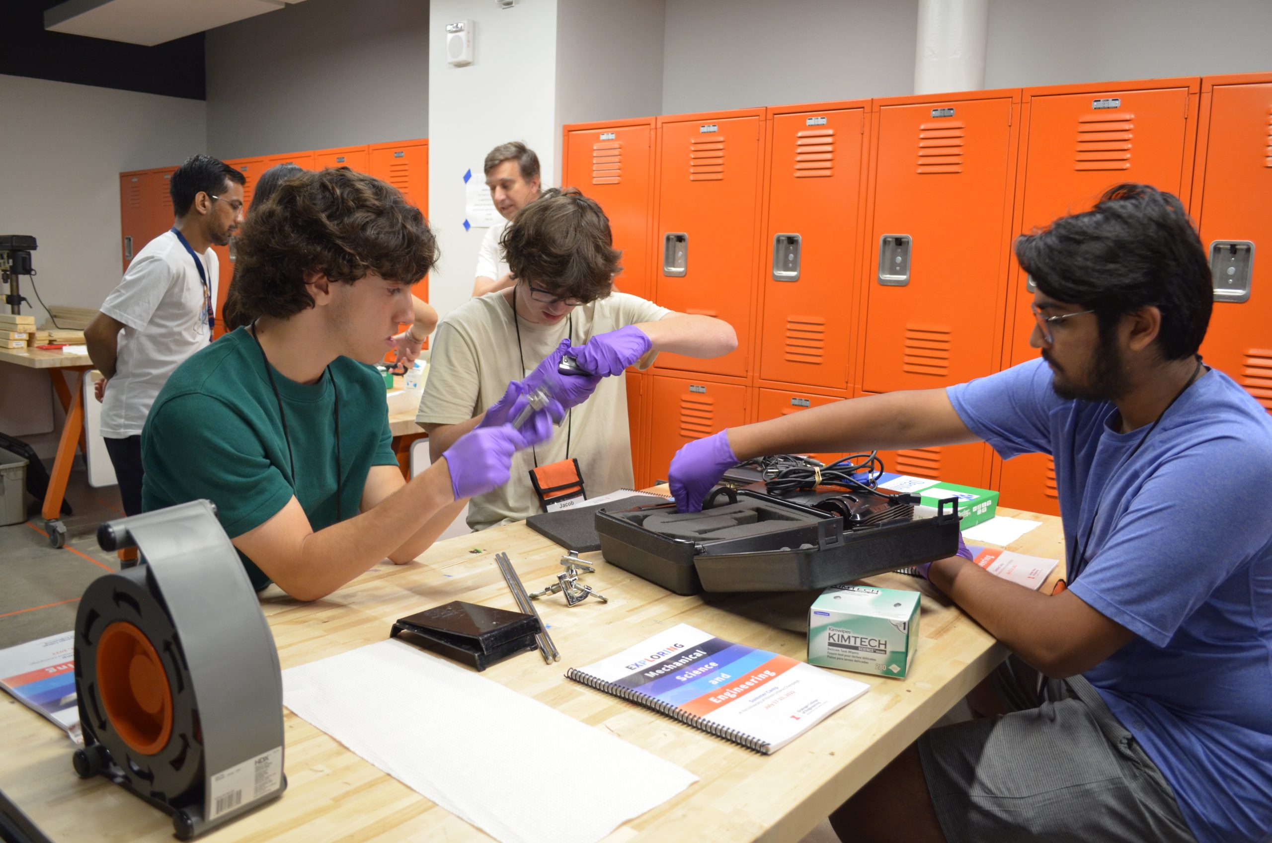 Campers sitting around a table, wearing gloves and working on a lab activity