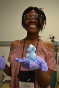 Camper smiling at camera wearing protective goggles and gloves, holding some material